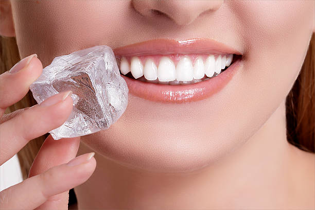 A woman smiles as she holds a cube of ice near her teeth.